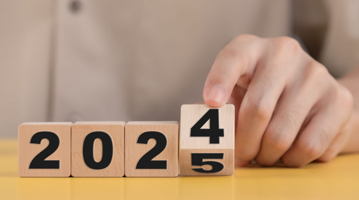 Foto de quatro cubos de madeira, cada um com um número formando 2025 em sequência. Uma mão humana segura o último bloco como se quisesse movê-lo do número 4 para o 5.